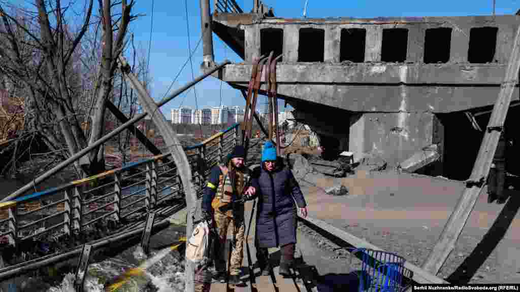 Боєць територіальної оборони (ТРо є складовою ЗСУ) допомагає жінці перейти зруйнований міст під час евакуації з міста Ірпінь. Київщина, березень 2022 року