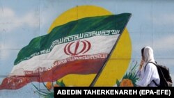 O femeie trece pe lângă un steag al Iranului în Teheran. Protestele din Iran continuă în 2023, însă sunt ridicate semne de întrebare despre supraviețuirea mișcării. 