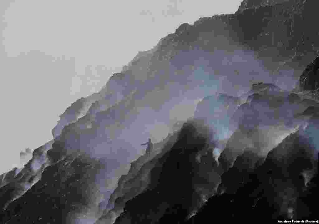 Зьбіральнік адкідаў спускаецца па гары сьмецьця, якое тлее на палігоне Бхалсва, у Сусьветны дзень навакольнага асяродзьдзя ў Нью-Дэлі, Індыя, 5 чэрвеня 2022