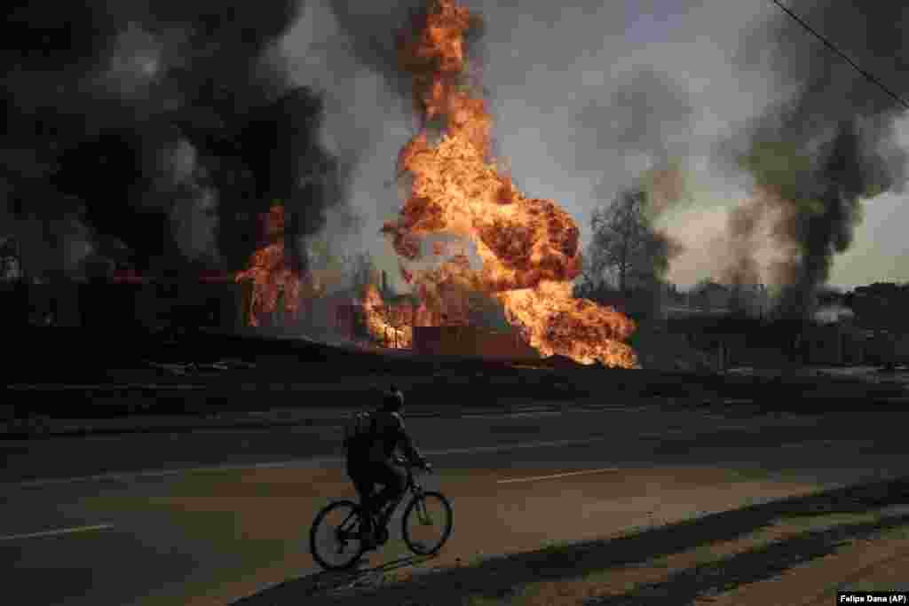 A man rides his bike past flames and smoke rising from a fire following a Russian attack in Kharkiv on March 25, 2022.