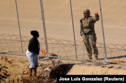 Osoba koji traži azil hoda ispred žičane ograde, dok pripadnik Teksaške nacionalne garde čuva stražu na obali rijeke Rio Bravo, granice između Sjedinjenih Država i Meksika, sa svrhom jačanja granične sigurnosti i sprječavanja prelaska migranata u Sjedinjene Države, u Ciudad Juarezu, Meksiko 9. januara 2023.