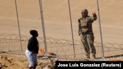 Një migrante në kufirin mes Shteteve të Bashkuara dhe Meksikës, si dhe një pjesëtar i Gardës Kombëtare të Teksasit.