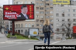 Egy nő egy belgrádi óriásplakát mellett, rajta Hszi Csin-ping kínai elnökkel. A feliraton ez áll: „Köszönöm, Hszi testvér!”