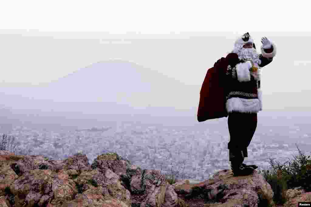 Исса Кассиси, одетый как Санта-Клаус, машет рукой и позирует представителям СМИ, стоя на горе Пропасть перед горой Фавор недалеко от Назарета, север Израиля, 12 декабря.