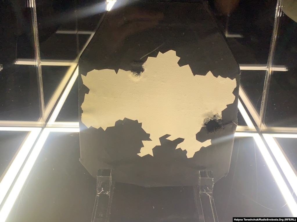 Një pllakë Kevlar e dëmtuar nga beteja, me një hartë të Ukrainës.     Organizatorët e ekspozitës thonë se synojnë të mbledhin para nga shitja e veprave të artit për të blerë më shumë jelekë antiplumb për trupat ukrainase. 