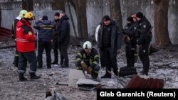 Adatdan daşary ýagdaýlar gullugynyň işgärleri we polisiýa ofiserleri 14-nji dekabrda Kiýewde rus dron hüjümi bilen ýykylan binada dronyň böleklerini gözden geçirýär. 