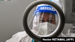Здравен работник изчаква хора да вземат проби от тампони за изследване за коронавирус в Шанхай на 23 декември 2022 г. 