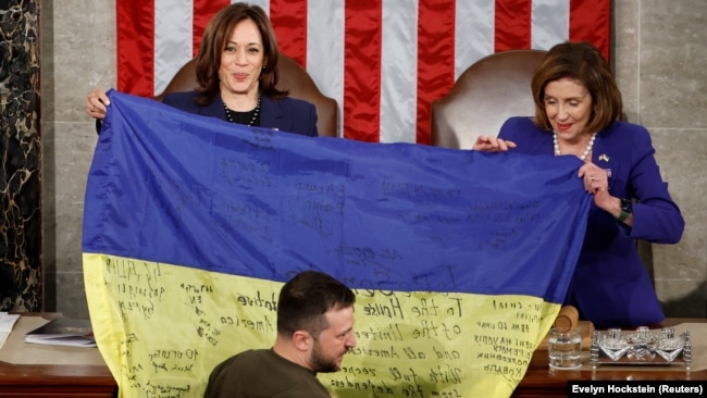 Вицепрезидентката Камала Харис (вляво) и председателката на долната камара на американския парламент Нанси Пелоси вдигат украинското знаме преди речта на украинския президент Володимир Зеленски. 21 декември 2022 г.