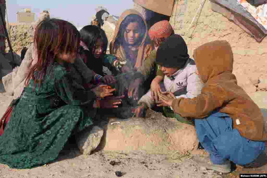 Afghan internally displaced children warm up around a fire outside their temporary mud house on the outskirts of Herat Province.