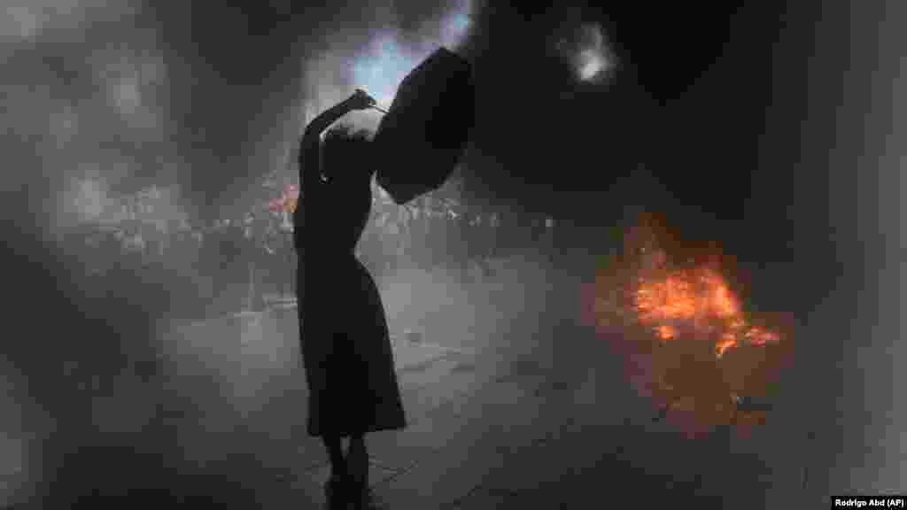 Женщина, выкрикивающая антиправительственные лозунги, стоит с зонтом на фоне черного дыма во время демонстрации в Буэнос-Айресе, Аргентина, 10 марта 2022 года. Аргентинцы вышли на улицы в знак протеста против соглашения правительства с Международным валютным фондом о рефинансировании долга на сумму около 45 миллиардов долларов&nbsp;
