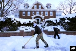 Doi copii curăță zăpada pe o stradă din Minneapolis, SUA, pe 22 decembrie 2022.