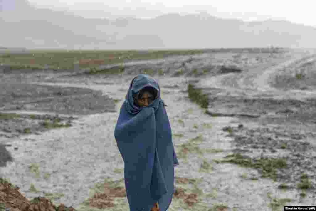 A 9-year-old Afghan girl covers herself during a downpour at the brick factory where she works.