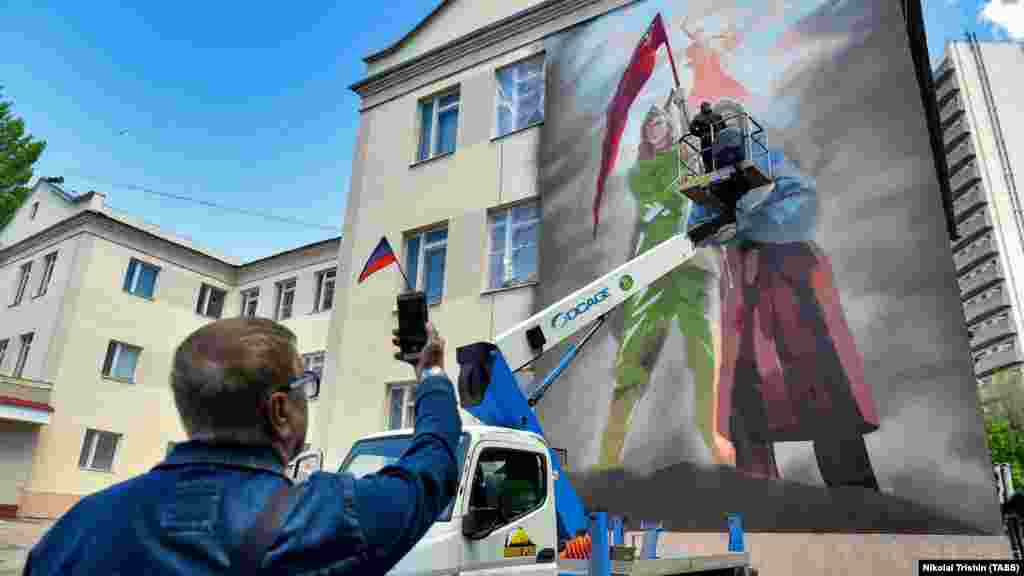Художник работи върху стенопис, свързващ Втората световна война с руската инвазия в Украйна в окупирания от Русия украински град Донецк през май.