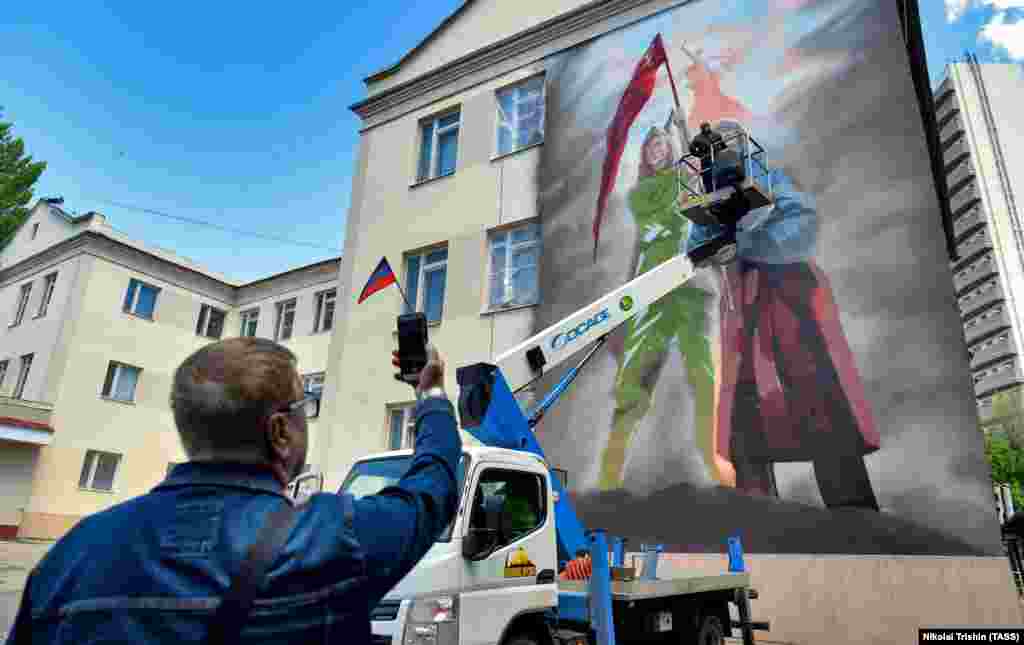 Një piktor punon në një mural që lidh Luftën e Dytë Botërore me pushtimin rus të Ukrainës, në qytetin ukrainas të Donjeckut të pushtuar nga Rusia në maj. &nbsp;