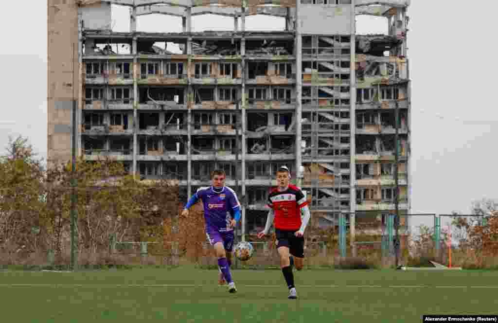 Futbolcılar büyük zarar körgen bina ögünde idman ete. Oktâbrniñ 30-nda Reuters agentligi derc etken fotoresimler Rusiye işğal etken Mariupoldeki yaşayışnı köstere.