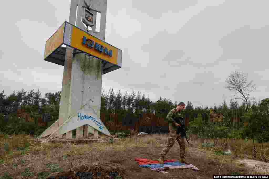 Стела міста Ізюму (вʼїзд з боку Харкова) поруч на землі лежить російський прапор.&nbsp;Охочі фотографуються на ньому та витирають об нього ноги, вересень 2022 року / Праворуч: жовтень 2024-го