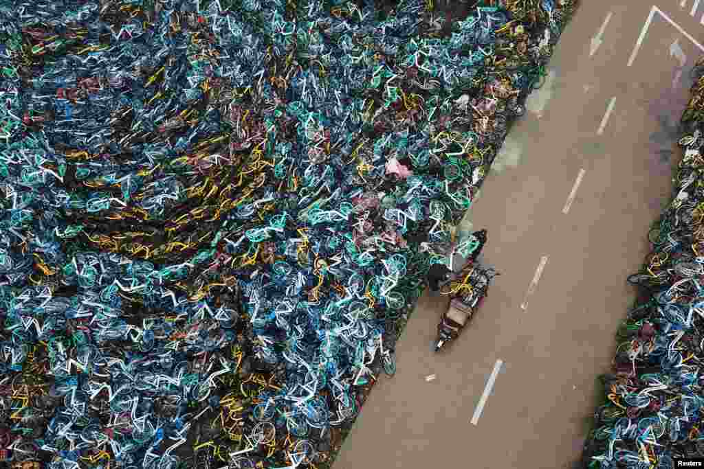Urban-management officers transport a bicycle next to piled-up bicycles of bike-sharing services in Hefei in China's Anhui Province. (Reuters)