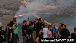 People flash the victory gesture as they pose for a "selfie" photo on a cell phone while others watch as fires blaze along the Lebanese side of the border with Israel in the Lebanese village of Maroun al-Ras on September 1, 2019