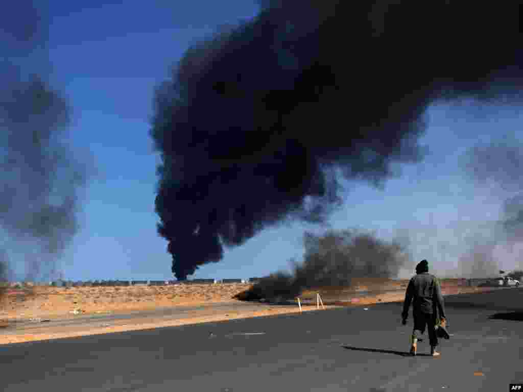 A Libyan rebel fighter walks barefoot near burning tires as smoke rises from an oil refinery storage tank near the oil port of Ras Lanuf. Photo by Roberto Schmidt for AFP