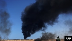 A rebel fighter walks past as smoke rises from an oil refinery storage tank near Ras Lanouf.