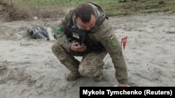 Украинский военный сапер поднимает неразорвавшуюся часть кассетной бомбы.

