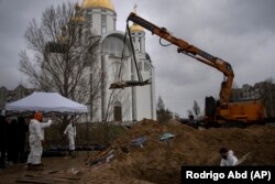 Кран поднимает труп мужчины из братской могилы в Буче на окраине Киева. Тела погибших исследуют в морге, позже перезахоронят. Украина, 10 апреля 2022 года