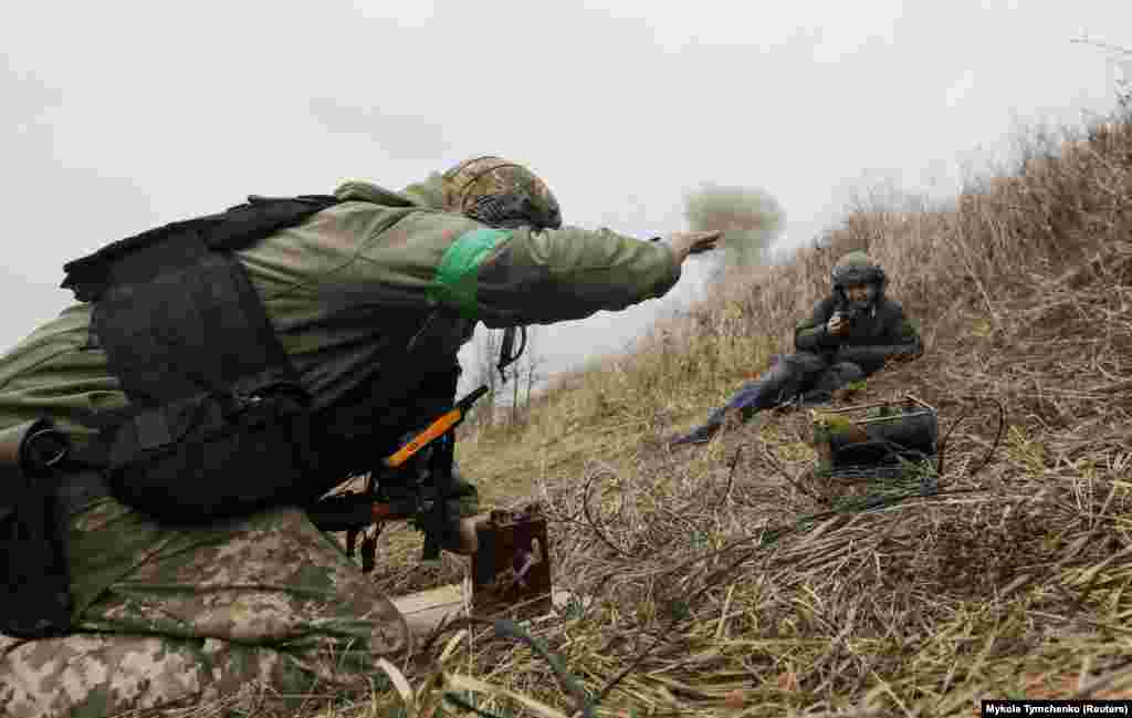 A photographer looks on as a Ukrainian sapper detonates a pile of munitions that were uncovered in and around&nbsp;Motyzhyn on April 10.&nbsp;