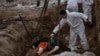 Un muncitor al cimitirului mută un cadavru dintr-o groapă comună din Bucea pe o macara pentru a-l duce la morgă, la identificare