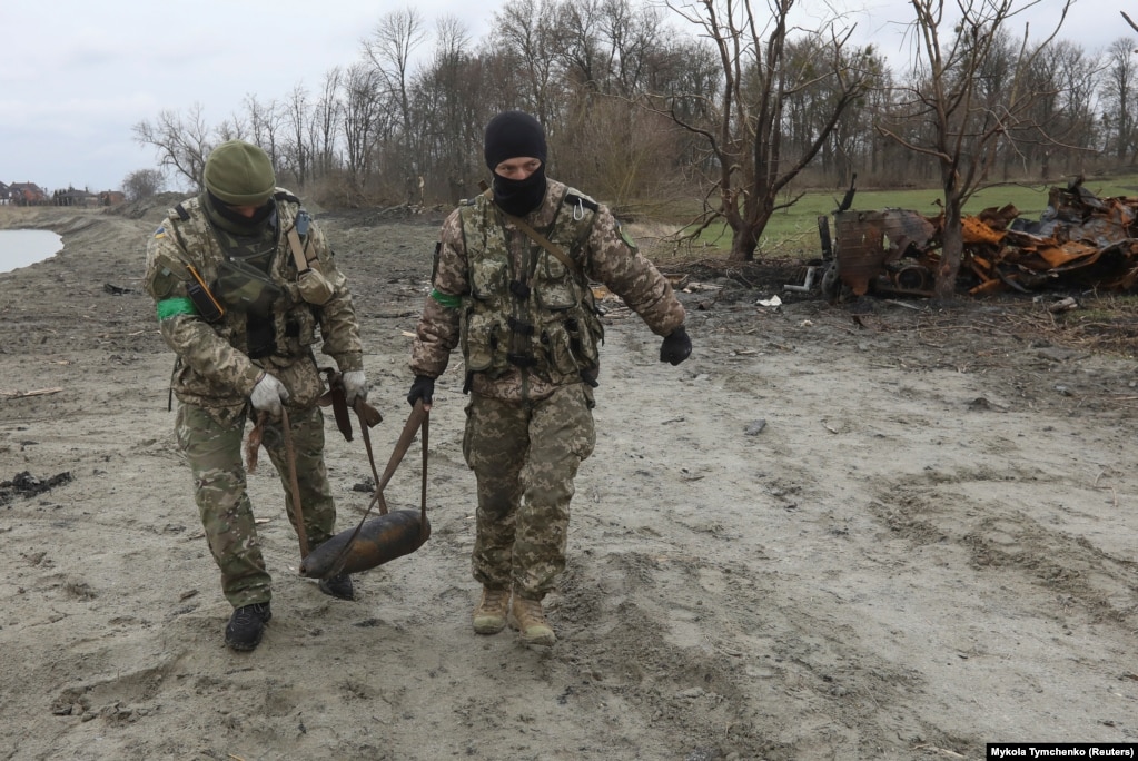 Ushtarët ukrainas mbajnë një predhë të pashpërthyer afër Motizhinit - një fshat në perëndim të Kievit, më 10 prill.