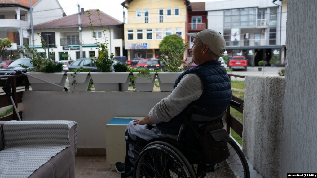 Ibrahim Hetemi, përdorues i karrocës duke qëndruar në ballkonin e shtëpisë së tij.