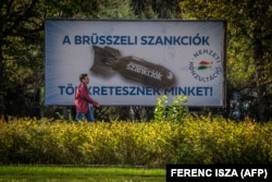 Un bărbat trece pe lângă un panou stradal care înfățișează o bombă pe care scrie „Suntem pedepsiți de sancțiunile de la Bruxelles”, în Budapesta, pe 18 octombrie 2022.