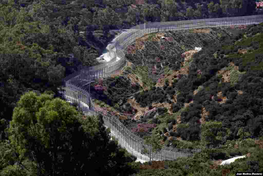 Gardul de frontieră care separă micul teritoriu nord-african al Spaniei, Ceuta, de Maroc, iunie 2018. Gardul este format din două bariere înalte de 6 metri, acoperite cu sârmă ghimpată. O serie de senzori de zgomot și de mișcare completează eforturile sutelor de polițiști care patrulează bariera.