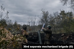 Українські вояки завантажують міну до міномета калібру 120 міліметрів, готуючись зробити постріл в бік російських позицій на Донбасі. Жовтень 2022 року