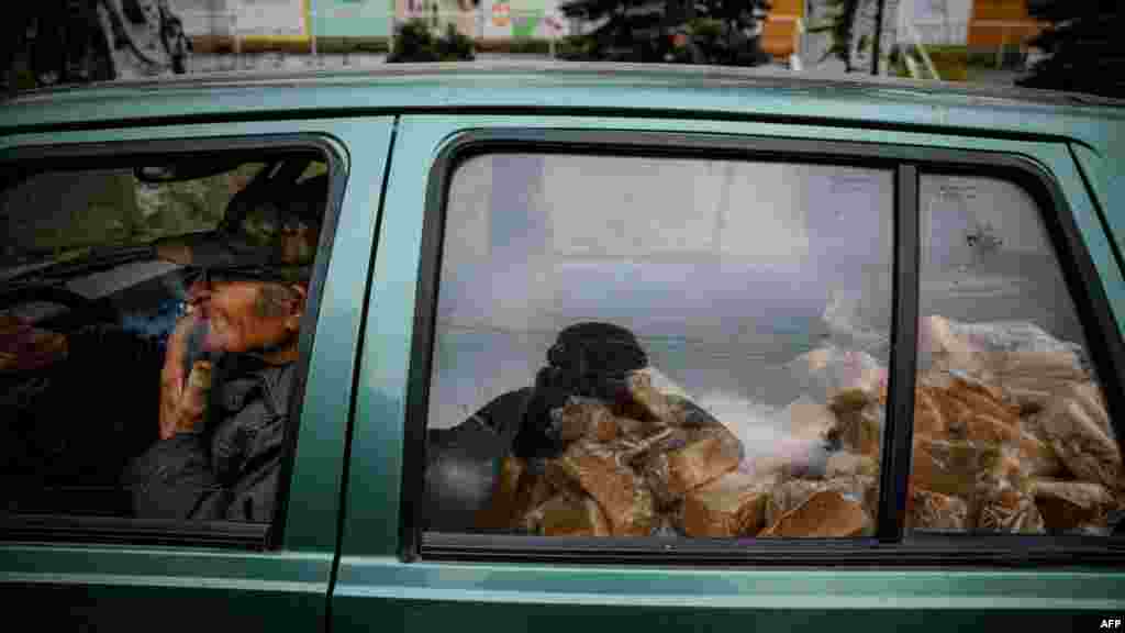 Egy idős önkéntes cigarettaszünetet tart, miközben autójával kenyeret szállít egy közeli faluba