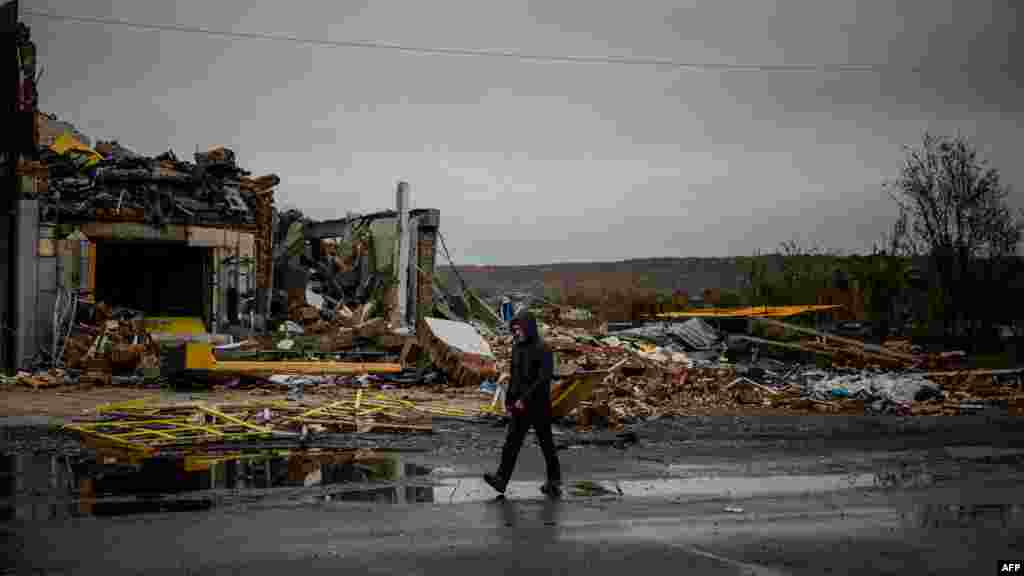 Egy helyi lakos siet az esőben egy szinte földig rombolt épület előtt