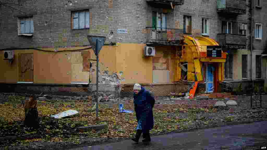 Egy idős nő egy megrongálódott lakóház előtt sétál a belvárosban