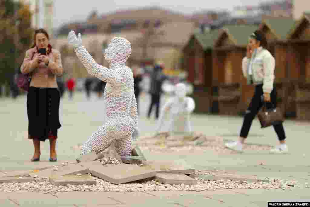 People walk between sculptures of an art installation created by Kosovar sculptor Eroll Murati titled Find Me, on display in the main square in Pristina to symbolize the missing person&#39;s plea for their bodies to be found. Some 1,600 people in Kosovo, most of them Albanians, are still listed as missing from the 1998-99 war.