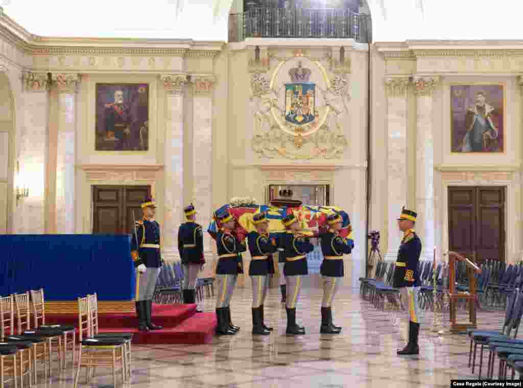 Sicriul cu trupul neînsuflețit al Regelui Mihai scos din Palatul Regal. Pe fundal, portretele Regelui Carol I și Ferdinand