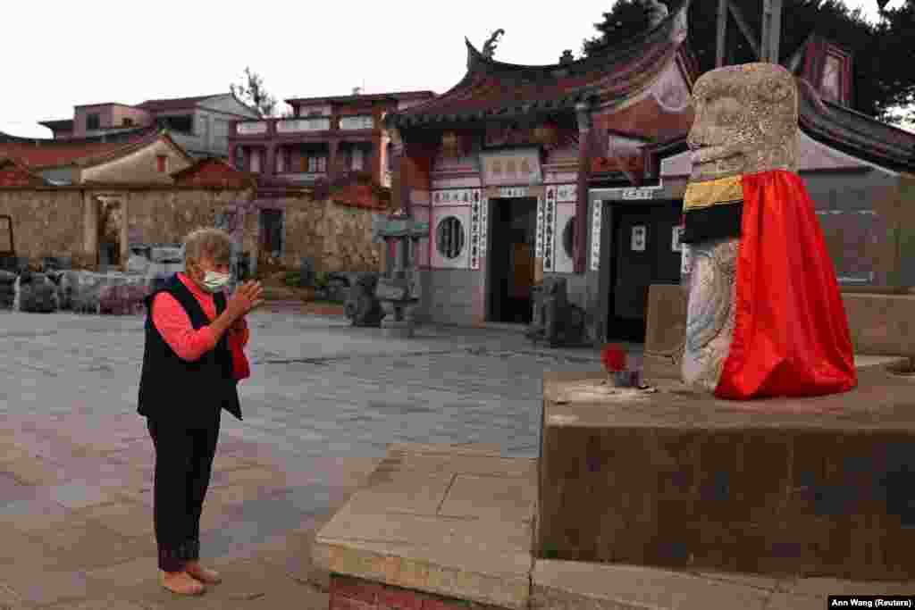 Egy nő imádkozik egy templom előtti oroszlánszobornál Csinmen egyik falujában