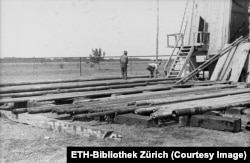 Workers with lengths of drill piping at the base of a derrick in Aricesti