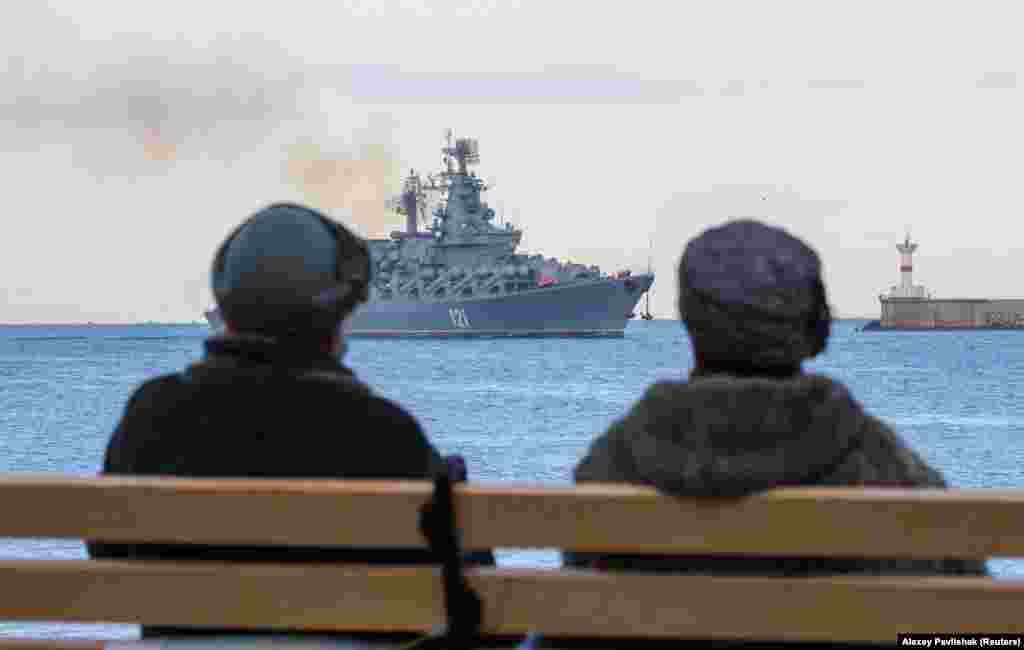 Women sit on a bench as the Russian Navy&#39;s guided missile cruiser Moskva sails back into harbor after tracking NATO warships in the Black Sea, in the port of Sevastopol, Crimea.