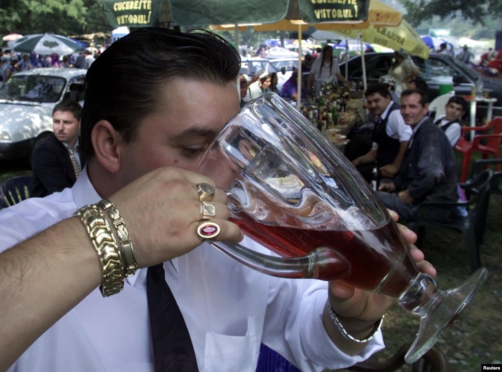 A Romany man chugs red wine from a pitcher at an open-air party in Costesti, west of Bucharest, in 2002.