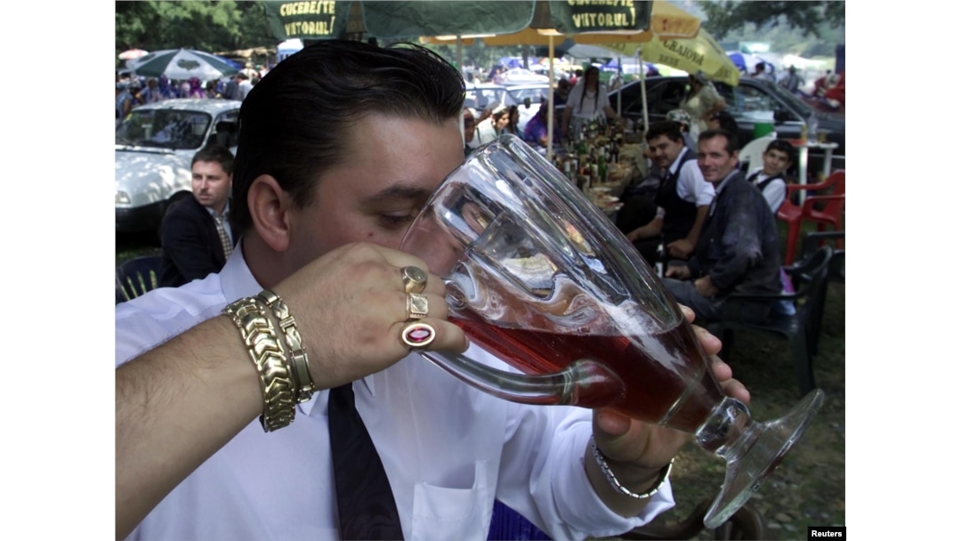 A Romany man chugs red wine from a pitcher at an open-air party in Costesti, west of Bucharest, in 2002.