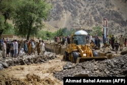 Villagers watch as a bulldozer cleans debris from a flood in the Khenj district of Panjshir Province on July 3.