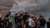 People flash the victory gesture as they pose for a "selfie" photo on a cell phone while others watch as fires blaze along the Lebanese side of the border with Israel in the Lebanese village of Maroun al-Ras on September 1, 2019