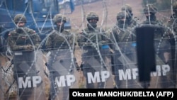 Polish servicemen stand behind a barbed-wire fence on the Belarusian-Polish border as they watch migrants camping near the city of Hrodna in Belarus. 