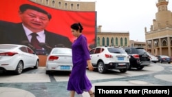 Женщина-уйгурка на улице в Кашгаре на фоне гигантского монитора с трансляцией выступления главы Китая Си Цзиньпина. 2018 года