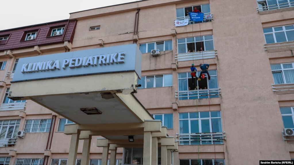 Dy alpinistë të veshur si mjekë lëshohen me litarë dhe argëtojnë fëmijët në Klinikën e Pediatrisë në Prishtinë.