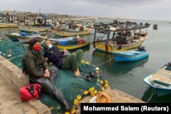 Pescarii palestinieni se odihnesc pe plase în timp ce bărcile sunt legate după ce Israelul a restricționat zona de pescuit palestiniană ca răspuns la rachetele palestiniene, în portul maritim al orașului Gaza, 26 aprilie 2021.