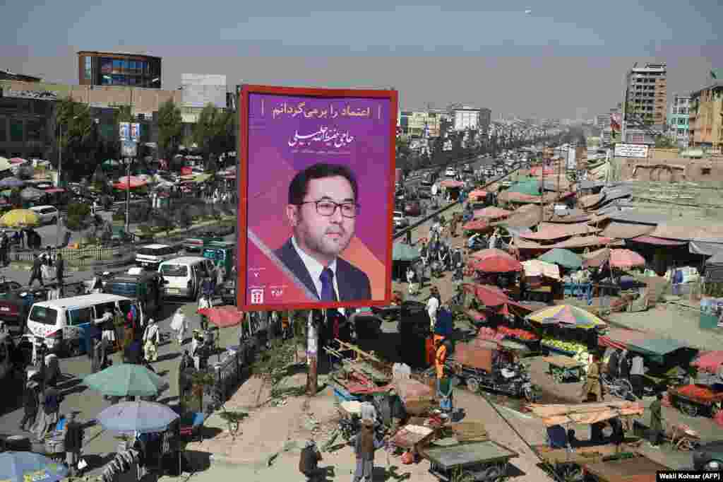 Afghan commuters and pedestrians are seen along a road in Kabul featuring a billboard of parliamentary candidate Haji Hafizullah Jalili. Campaigning for Afghanistan&#39;s long-delayed parliamentary elections kicked off on September 28. (AFP/Wakil Kohsar)